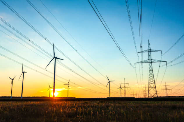 Hochspannungsleitungen mit Windkraftanlagen im Hintergrund bei Sonnenuntergang
